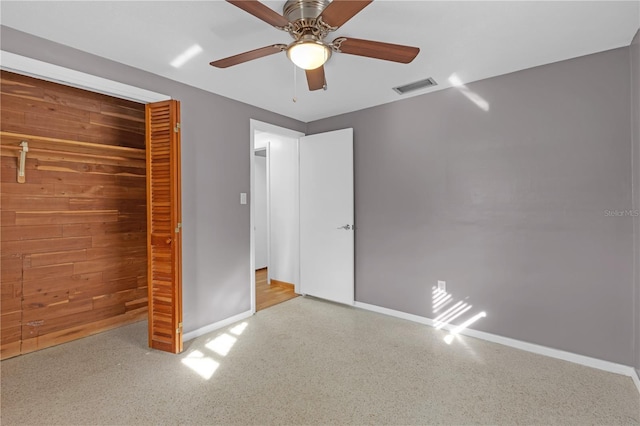 unfurnished bedroom featuring ceiling fan, a closet, and wood walls