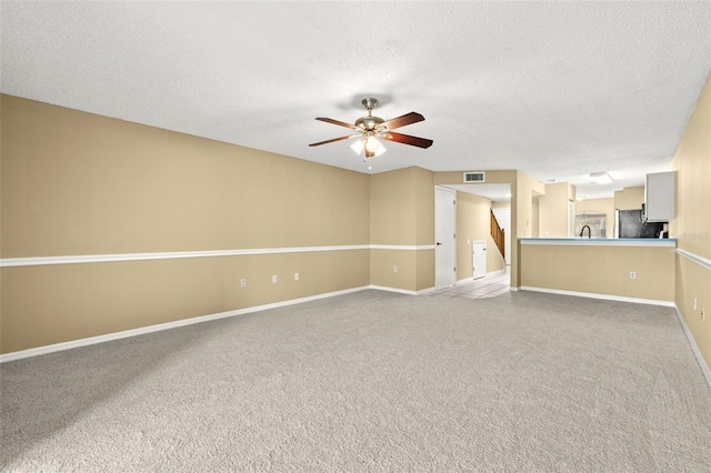 unfurnished living room with ceiling fan, carpet floors, and a textured ceiling