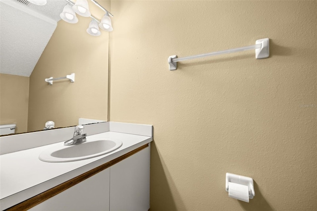 bathroom featuring a textured ceiling, vanity, toilet, and lofted ceiling