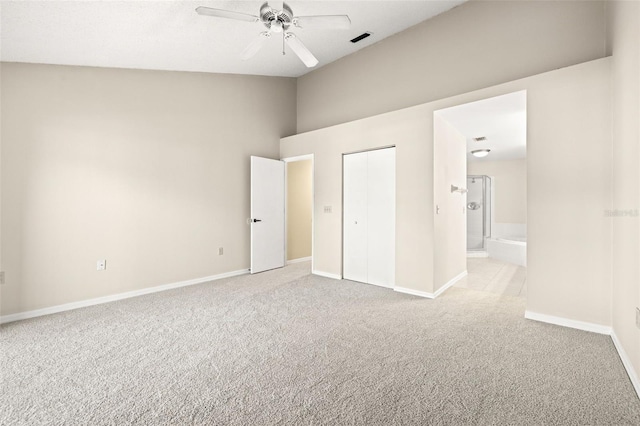 unfurnished bedroom with a closet, connected bathroom, light colored carpet, and ceiling fan