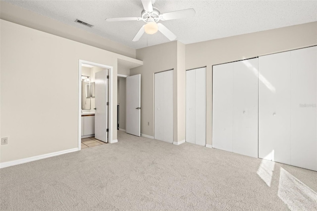 unfurnished bedroom featuring a textured ceiling, connected bathroom, ceiling fan, and two closets