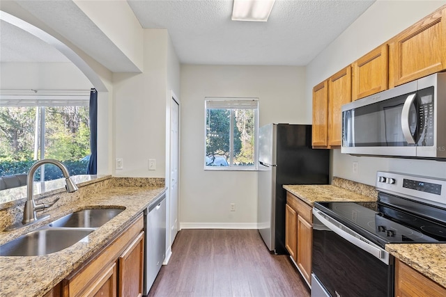 kitchen with sink, appliances with stainless steel finishes, dark hardwood / wood-style floors, light stone counters, and a textured ceiling