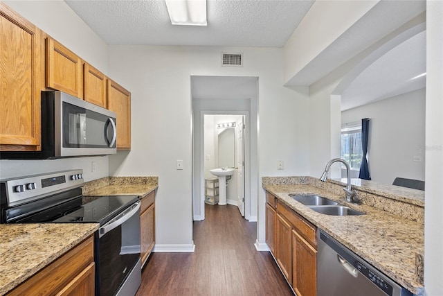 kitchen featuring sink, appliances with stainless steel finishes, dark hardwood / wood-style floors, light stone counters, and a textured ceiling