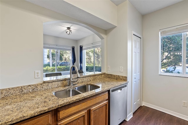 kitchen with stainless steel dishwasher, dark hardwood / wood-style floors, light stone countertops, and sink