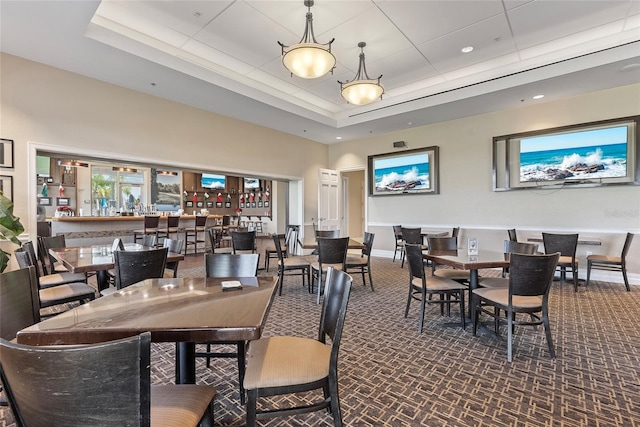 dining space featuring bar area, a raised ceiling, and dark colored carpet