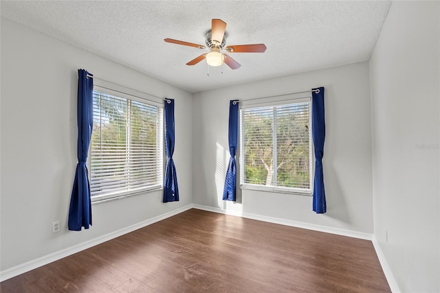 empty room featuring ceiling fan, a healthy amount of sunlight, a textured ceiling, and dark hardwood / wood-style flooring