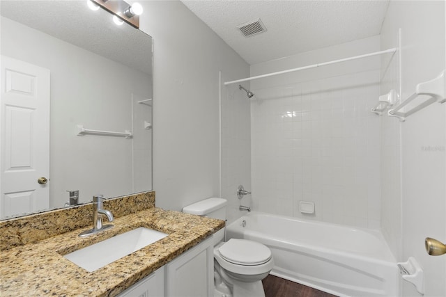 full bathroom featuring tiled shower / bath, hardwood / wood-style flooring, vanity, toilet, and a textured ceiling