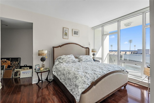 bedroom with dark hardwood / wood-style flooring, floor to ceiling windows, and a water view