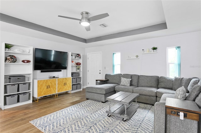 living room with hardwood / wood-style floors, ceiling fan, and a raised ceiling