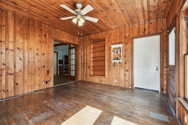 empty room featuring dark hardwood / wood-style flooring, wood ceiling, ceiling fan, built in features, and wood walls