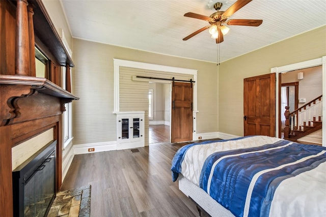 bedroom with ceiling fan, a barn door, and dark hardwood / wood-style flooring