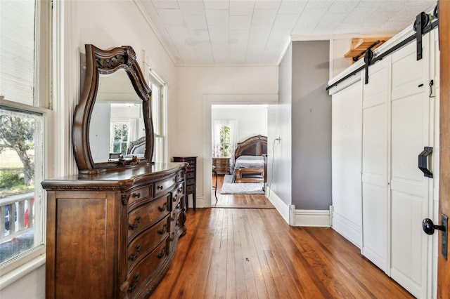 corridor with a barn door, crown molding, and dark wood-type flooring