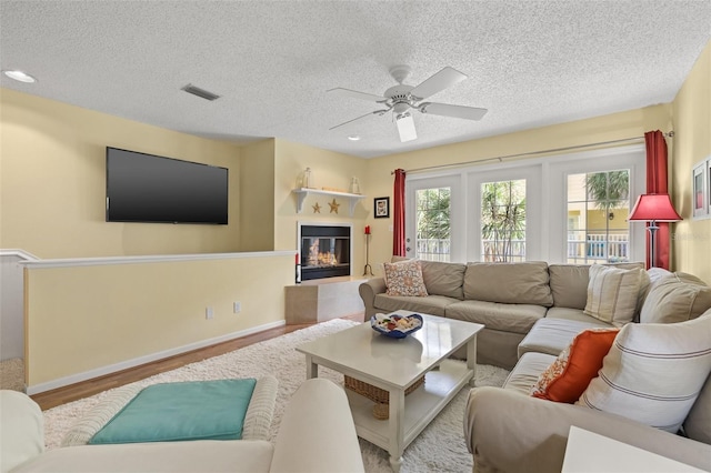 living room featuring ceiling fan, a textured ceiling, and light wood-type flooring