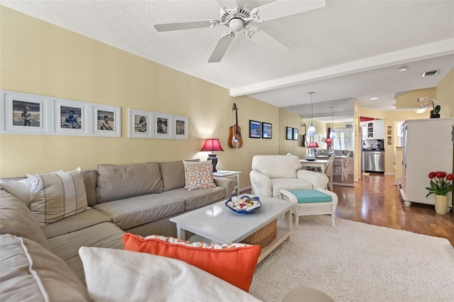 living room with beam ceiling, a textured ceiling, ceiling fan, and dark wood-type flooring