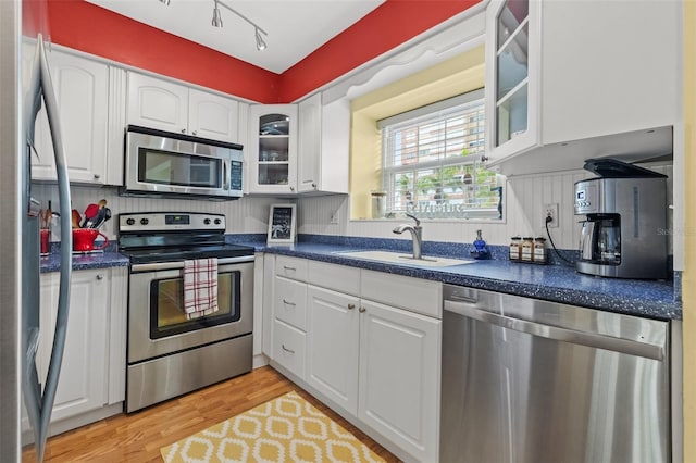 kitchen with sink, stainless steel appliances, white cabinetry, and light hardwood / wood-style flooring