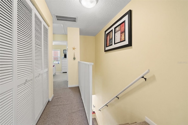 hall with a textured ceiling and light colored carpet