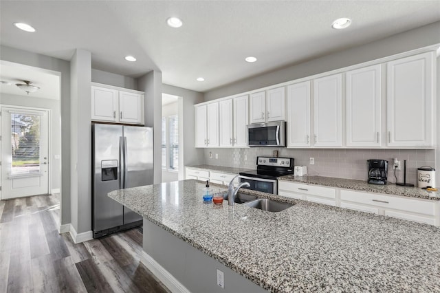 kitchen with a wealth of natural light, light stone countertops, stainless steel appliances, tasteful backsplash, and white cabinets