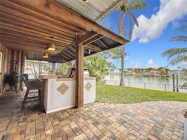 view of patio featuring exterior kitchen, grilling area, exterior bar, and a water view