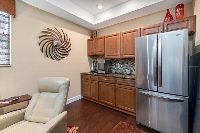 kitchen with tasteful backsplash, stainless steel fridge, dark wood-type flooring, and dark stone countertops