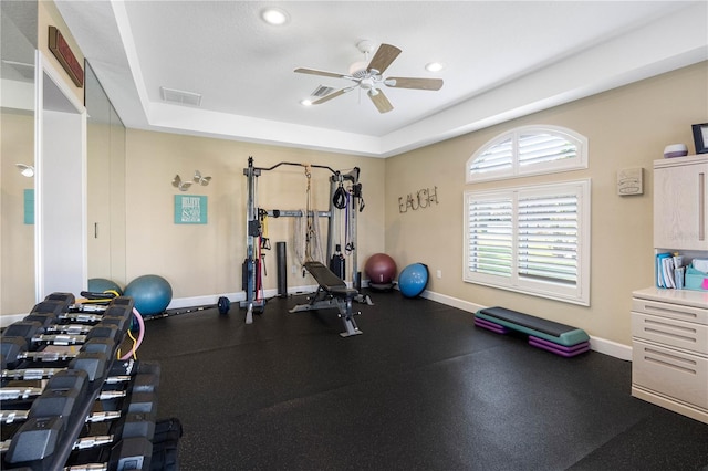 workout room featuring a raised ceiling and ceiling fan