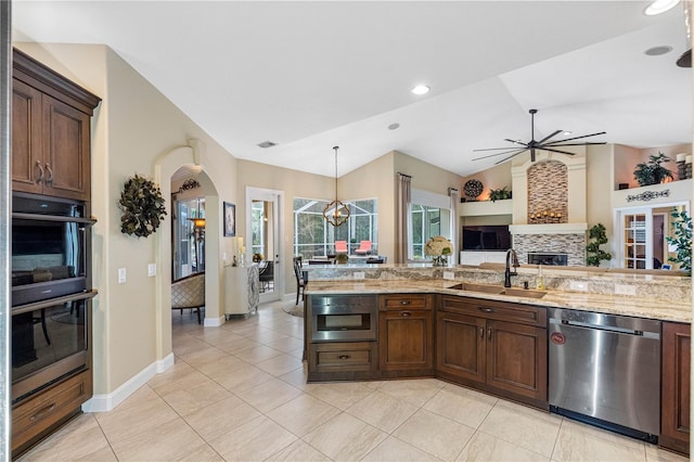 kitchen with appliances with stainless steel finishes, decorative light fixtures, sink, a tiled fireplace, and light stone counters