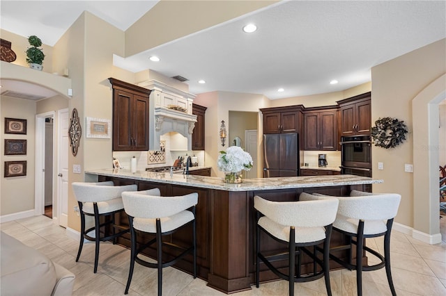 kitchen with a breakfast bar area, appliances with stainless steel finishes, dark brown cabinetry, light stone countertops, and kitchen peninsula