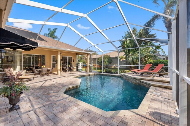 view of pool with ceiling fan, glass enclosure, and a patio area