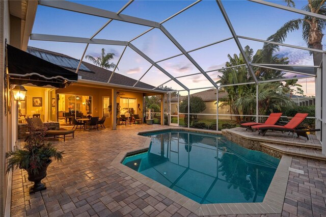 pool at dusk with glass enclosure and a patio area