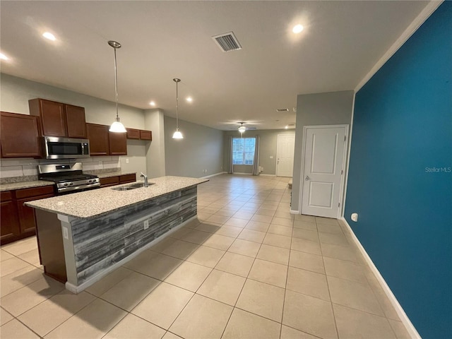 kitchen with appliances with stainless steel finishes, light tile patterned floors, a kitchen island with sink, and sink