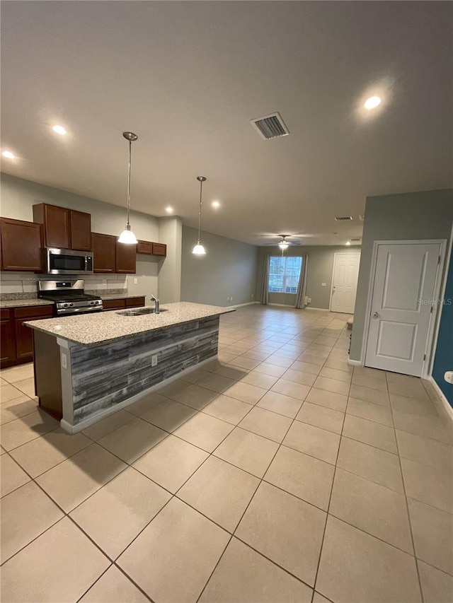 kitchen featuring an island with sink, pendant lighting, light tile patterned floors, and stainless steel appliances