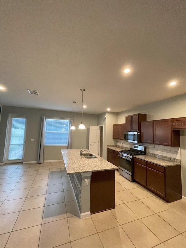 kitchen with a kitchen island with sink, sink, light tile patterned floors, decorative light fixtures, and stainless steel appliances