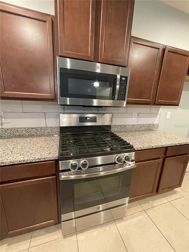 kitchen with light stone counters, light tile patterned floors, backsplash, and appliances with stainless steel finishes