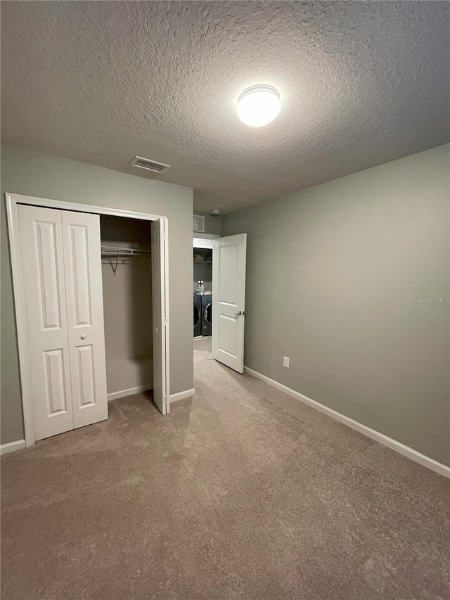 unfurnished bedroom featuring a closet, light colored carpet, washer and dryer, and a textured ceiling