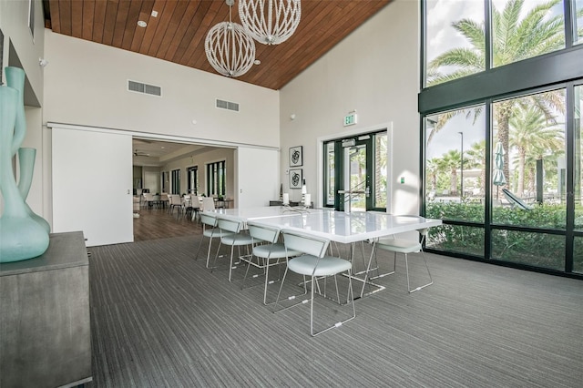 dining area featuring a notable chandelier, dark carpet, a towering ceiling, and wood ceiling