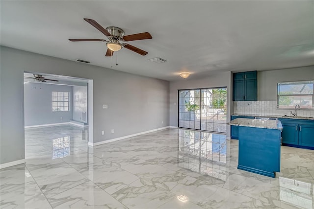 interior space with sink, ceiling fan, tasteful backsplash, a kitchen island, and light stone counters