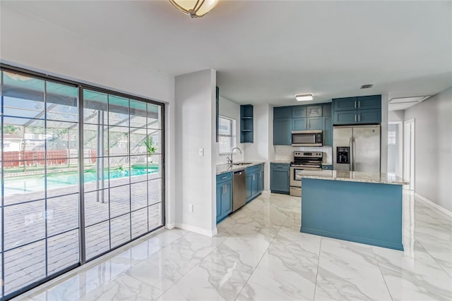 kitchen with sink, light stone counters, blue cabinets, decorative backsplash, and appliances with stainless steel finishes