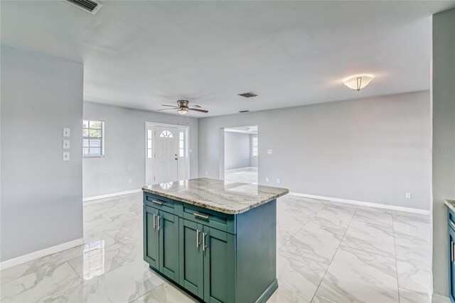 kitchen with green cabinets, light stone countertops, a center island, and ceiling fan