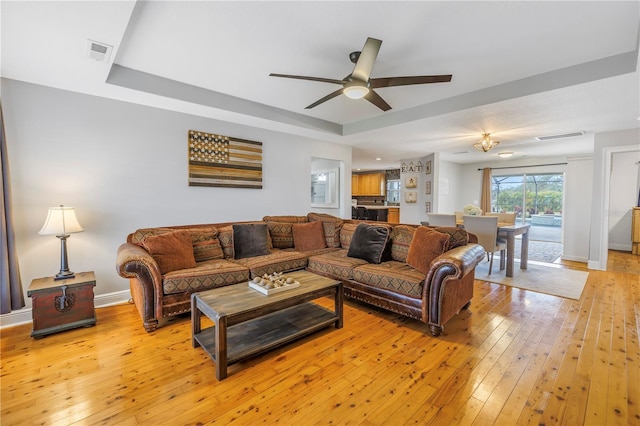 living room with light wood-type flooring, ceiling fan, and a raised ceiling