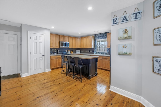 kitchen with a breakfast bar area, stainless steel appliances, decorative backsplash, light wood-type flooring, and a center island