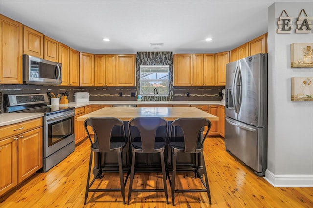 kitchen featuring a kitchen island, sink, light wood-type flooring, a kitchen breakfast bar, and stainless steel appliances