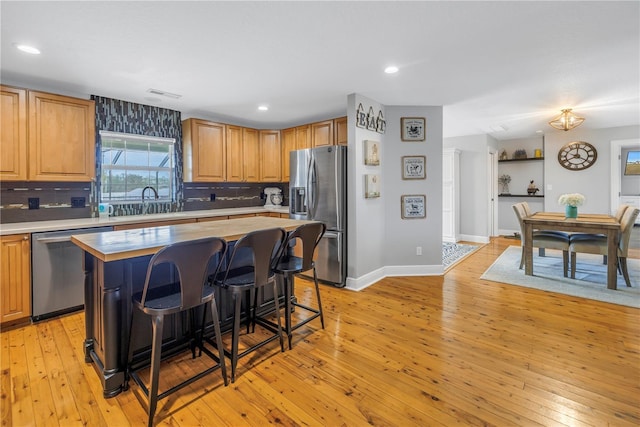 kitchen featuring light hardwood / wood-style floors, decorative backsplash, stainless steel appliances, and a center island