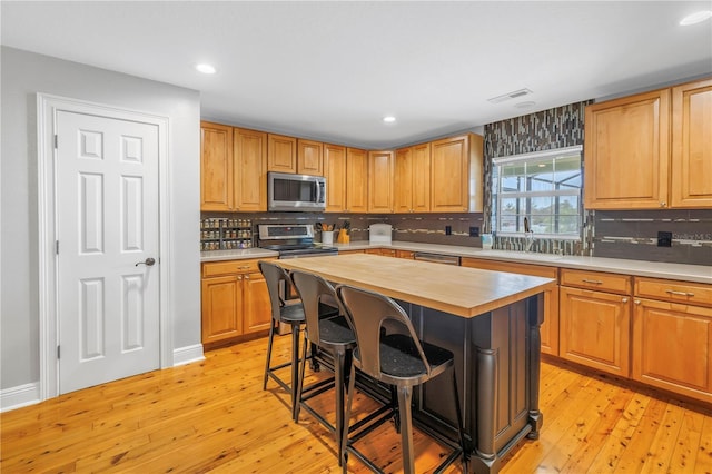 kitchen with a kitchen island, stainless steel appliances, sink, a breakfast bar, and light hardwood / wood-style flooring