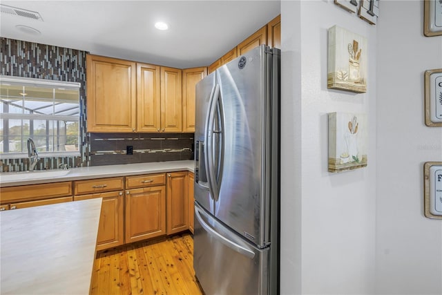 kitchen featuring stainless steel refrigerator with ice dispenser, tasteful backsplash, light wood-type flooring, and sink