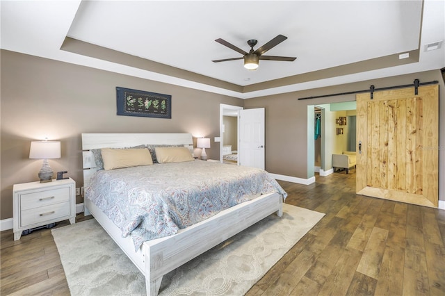 bedroom featuring ceiling fan, dark hardwood / wood-style floors, a raised ceiling, and a barn door