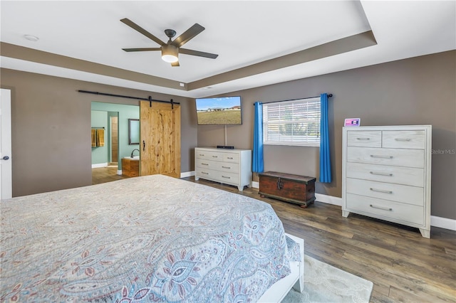 bedroom featuring ceiling fan, a barn door, dark hardwood / wood-style floors, and a tray ceiling