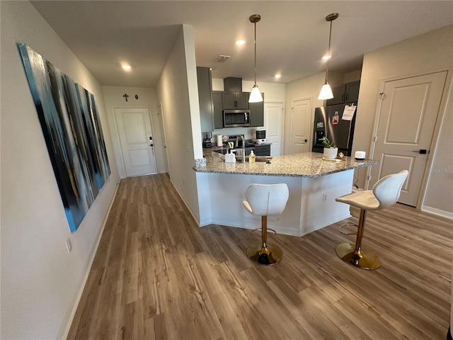 kitchen with sink, appliances with stainless steel finishes, light stone counters, kitchen peninsula, and a breakfast bar area