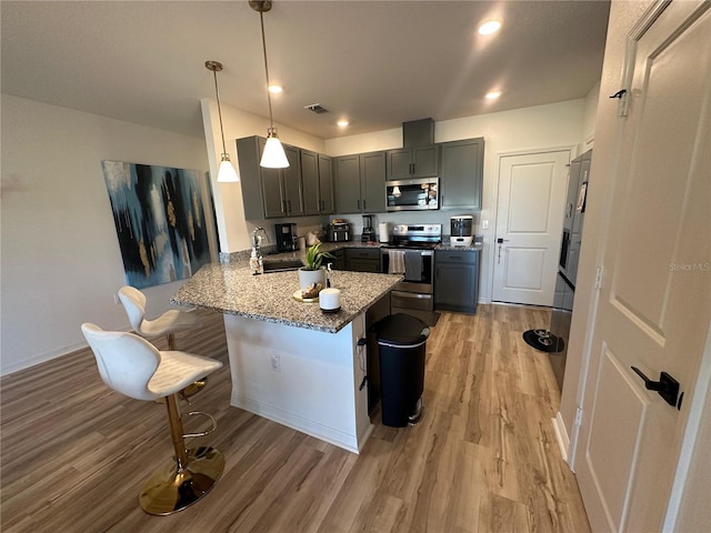 kitchen featuring pendant lighting, light stone countertops, a kitchen bar, kitchen peninsula, and stainless steel appliances