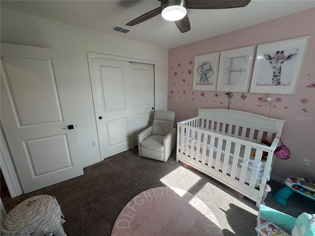 bedroom with dark colored carpet, ceiling fan, a crib, and a closet