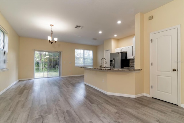 kitchen featuring white cabinetry, sink, hanging light fixtures, stainless steel fridge, and dark stone counters