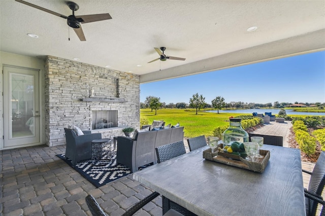 view of patio / terrace featuring an outdoor living space with a fireplace, a water view, and ceiling fan